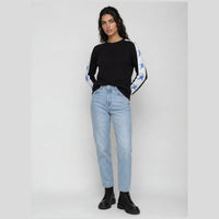 A woman modeling a black long-sleeve top with white and blue star-patterned sleeves, paired with light-wash blue jeans and black boots, against a light gray studio background.