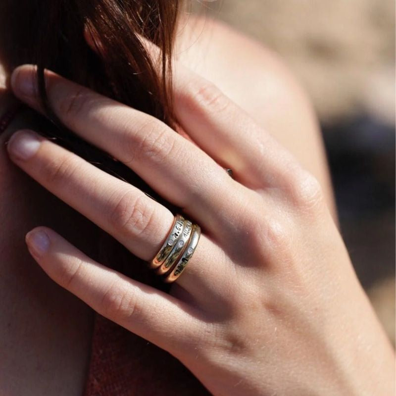 Close-up of a hand wearing a stack of rings on the index finger- including gold band inscribed with 'Light within '