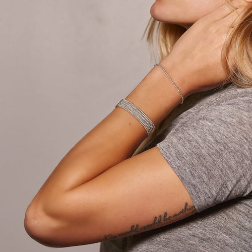 A stack of 2mm Silver ball bracelets  worn on the arm of a model wearing a grey t-shirt.