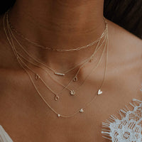 Horizon Necklace in  14k yellow gold with a bar set with 7 diamonds. . Shown in a stack on model with 4 other necklaces.