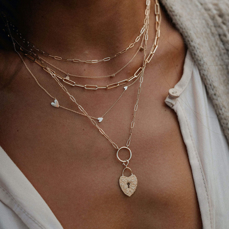 everyday love lineage heart necklace in 14k gold layered with other chains  on model 