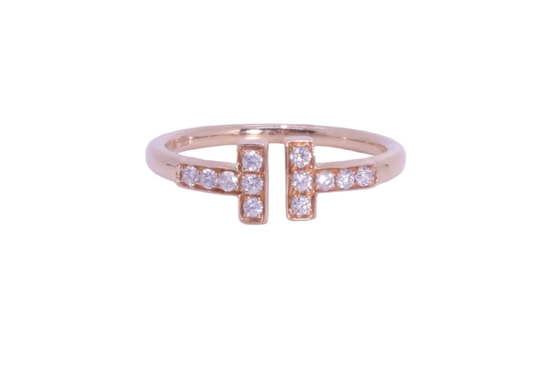 A rose gold ring with a split design, featuring small clear pavé diamonds on each side of a larger central diamond-studded bar, set against a plain light background.