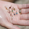 Hand holding a selection of ZAHAVA- Gemstone and Diamond Amulet Pendants set in 0 K Yellow Gold